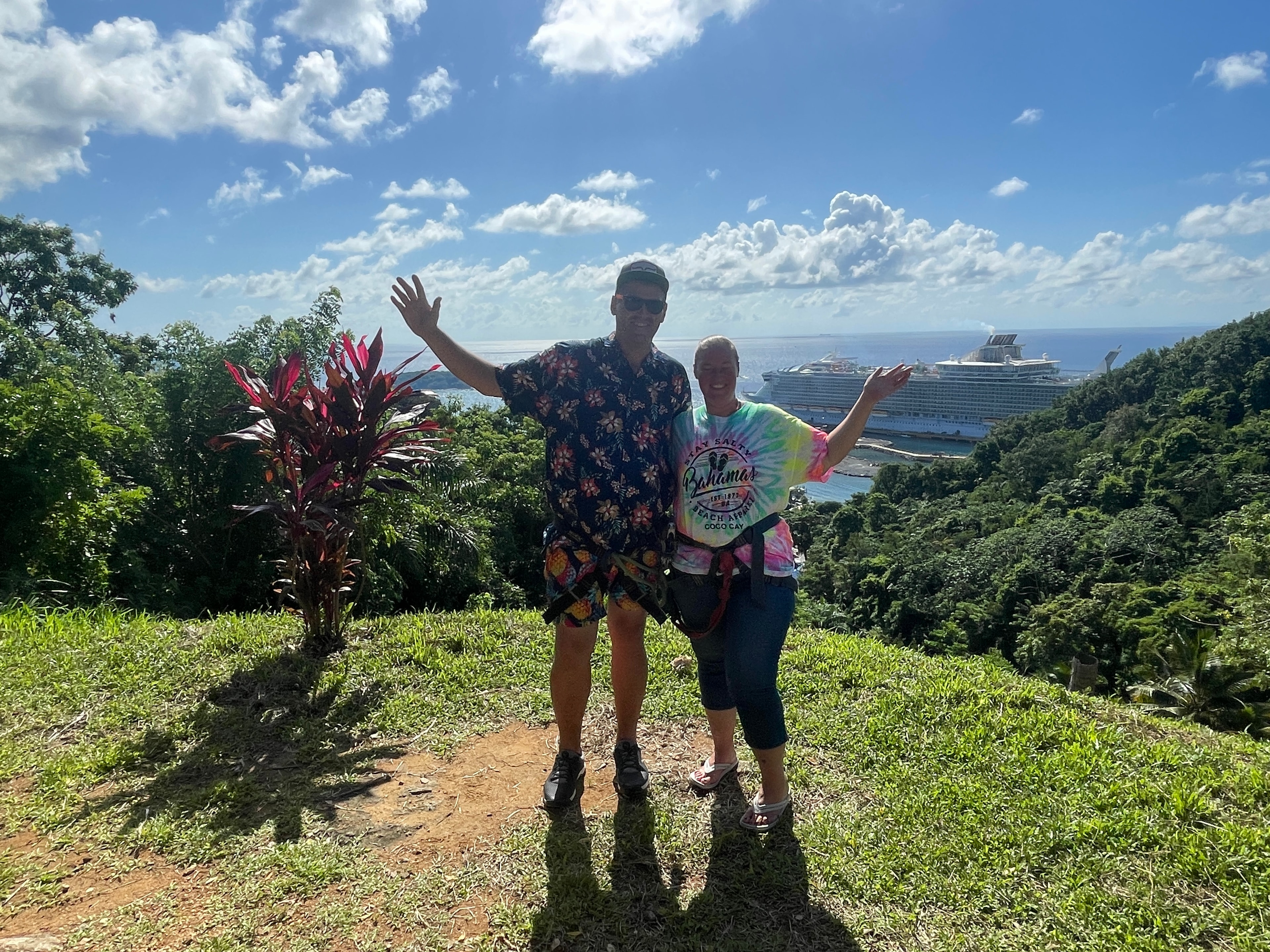 Couple celebrating on a tropical hilltop with cruise ship in background